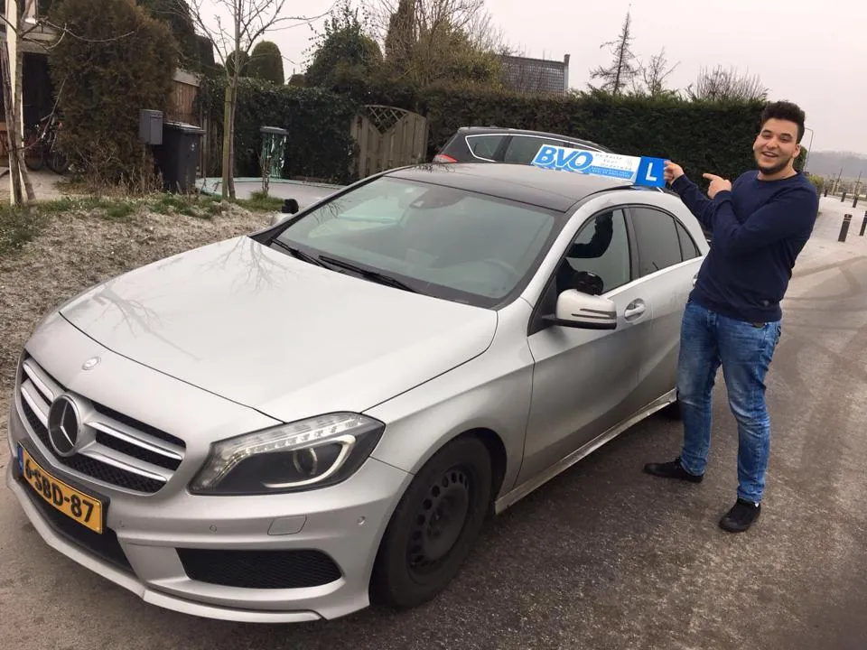 Geslaagde leerling wijst naar het BVO-daklicht op een lesauto